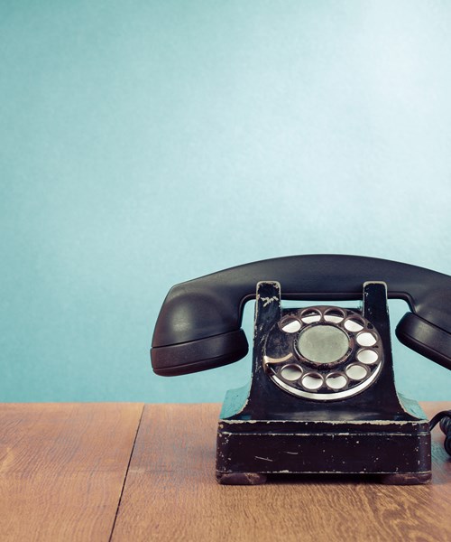 Image of old style black telephone on desk against a green background