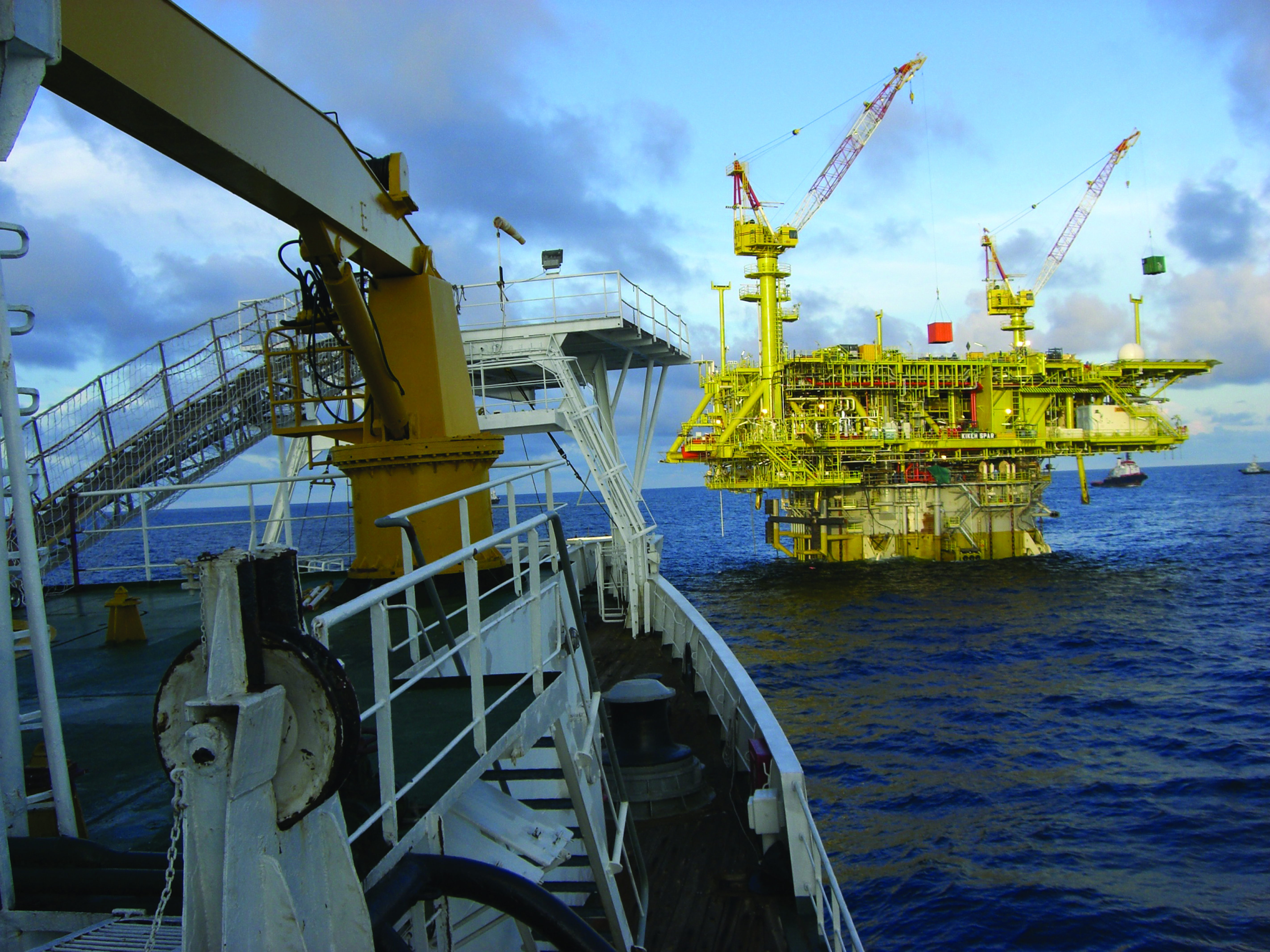 An image of an offshore oil and gas platform at sea with a vessel bow in the foreground