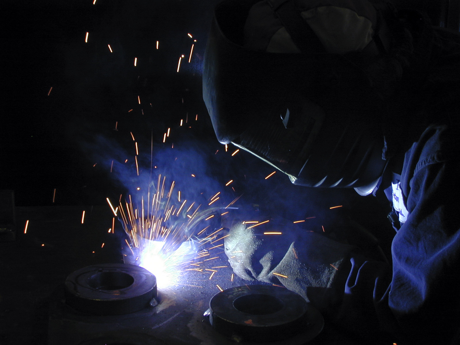 A welder wearing a helmet doing welding on a pipe